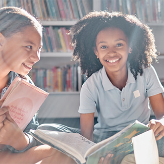 Two young people sit in a library holding books and smiling